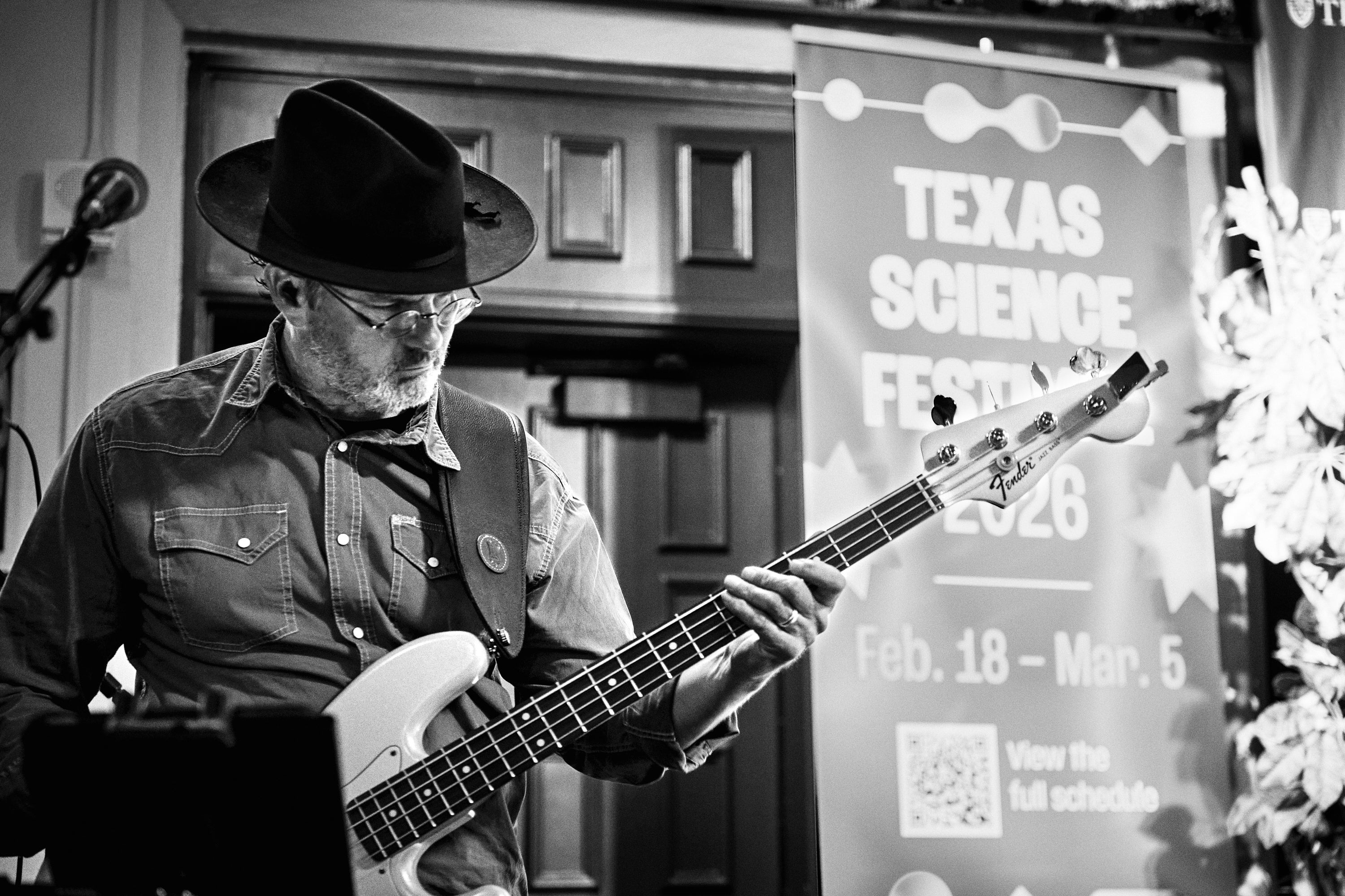 A guitarast in a hat plays in front of a banner that reads Texas Science Festival.